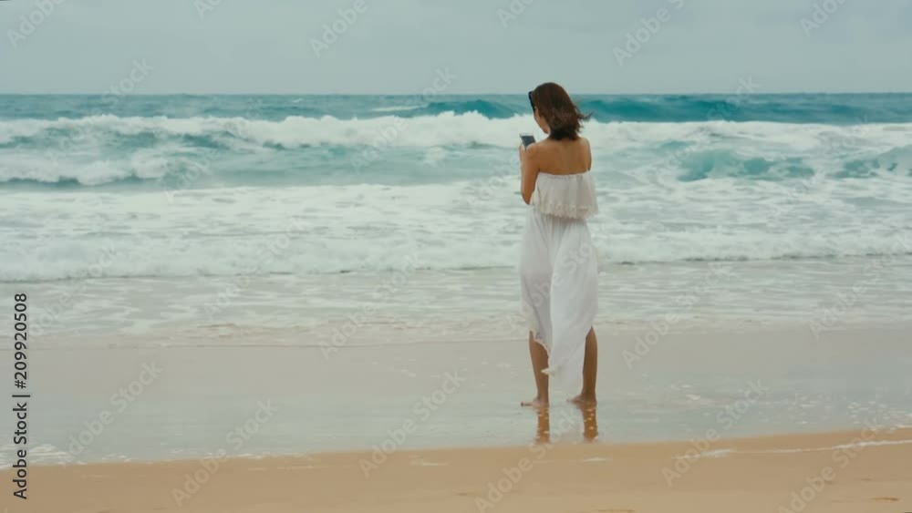 woman in white dress taking photos with her smartphone on beach woman in white dress taking photos with her smartphone on beach