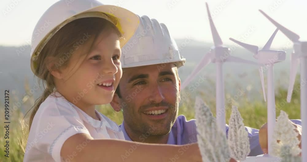 A father engineer shows his project to his daughter for the construction of a wind farm. The daughter is interested in renewable energy. Concept of: family, engineering, future love for nature.