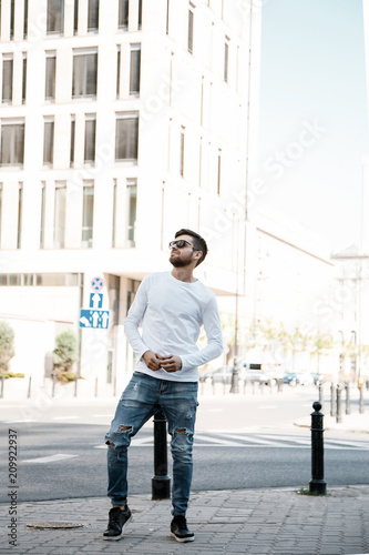 A young man travels through the streets of the city. Boy in sunglasses Stylish man near the building. The man sits on a whip. Beard and hair in a stylish guy. © ibilyk13