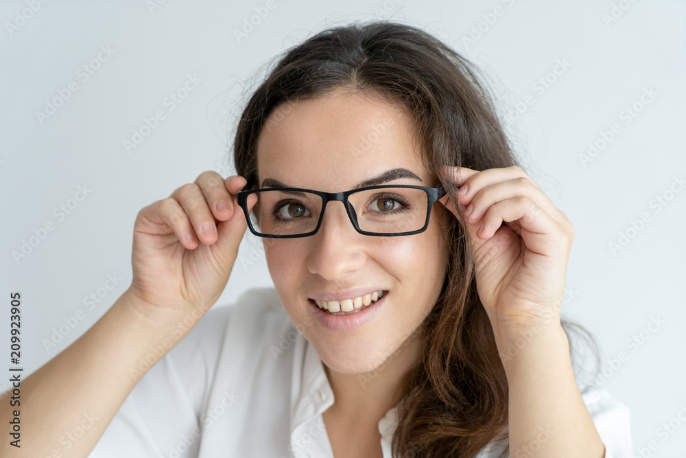 Amazed smiling girl trying on spectacles. Young Caucasian woman touching eyewear and looking through glasses. Vision and eye care concep