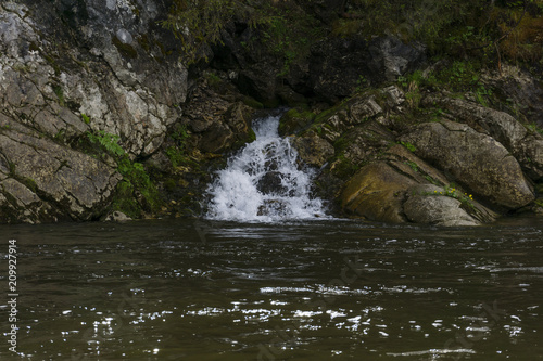 The spring follows a waterfall from the rock and flows into the river on a precipitous river bank..
