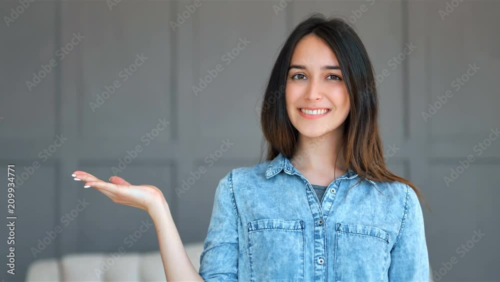 Happy woman presenting with open hand holding something blank indoors
