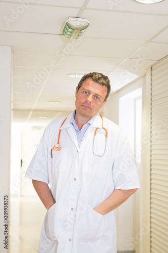 Smiling doctor posing with arms hands in the pockets in the office hospital wearing a stethoscope