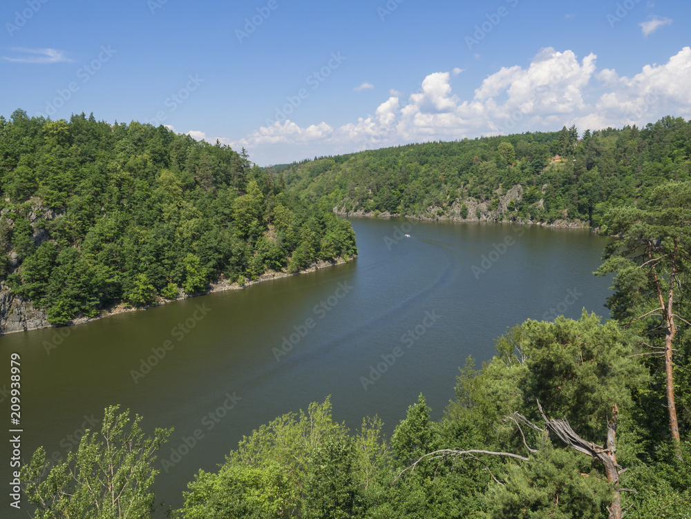 view from bridge zvikov on otava and vltava river with green tree forest rocky shore blue water, boat and blue sky white clouds background view from bridge zvikov on otava and vltava river with green tree forest rocky shore blue water, boat and blue sky white clouds background