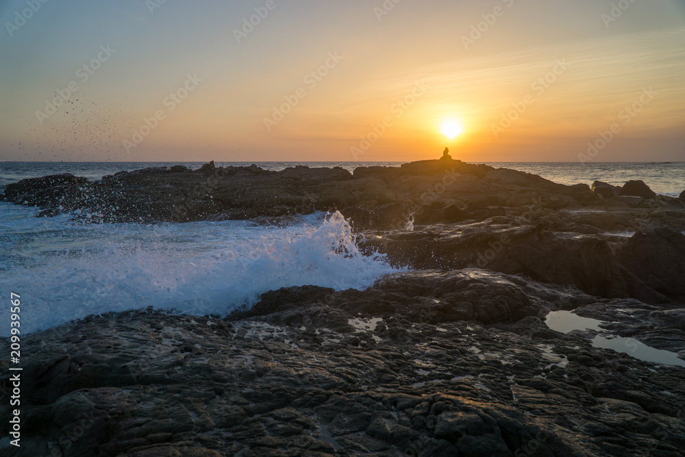 Fototapeta premium Women sitting on rocks at the beach with big waves.