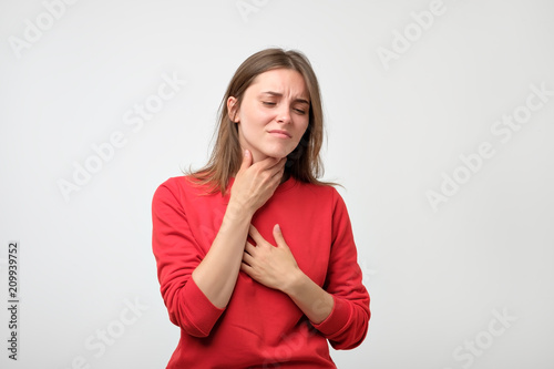 unhappy caucasian woman in red pulover suffering from throat pain at home