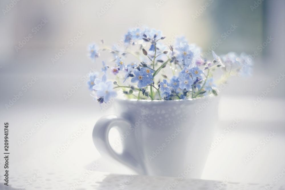 Blue flowers of a forget-me-not in a cup on a lacy tray. - obrazy, fototapety, plakaty 