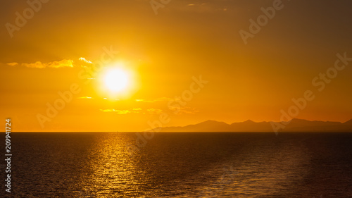 Lanzarote Sunset.  Sunset over the coastline of the Spanish Canary island of Lanzarote.  A yacht can be seen passing under the sun on the horizon.