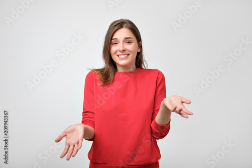 Studio portrait of attractive caucasian teenager in red pulover shrugging her shoulders having some doubts. photo