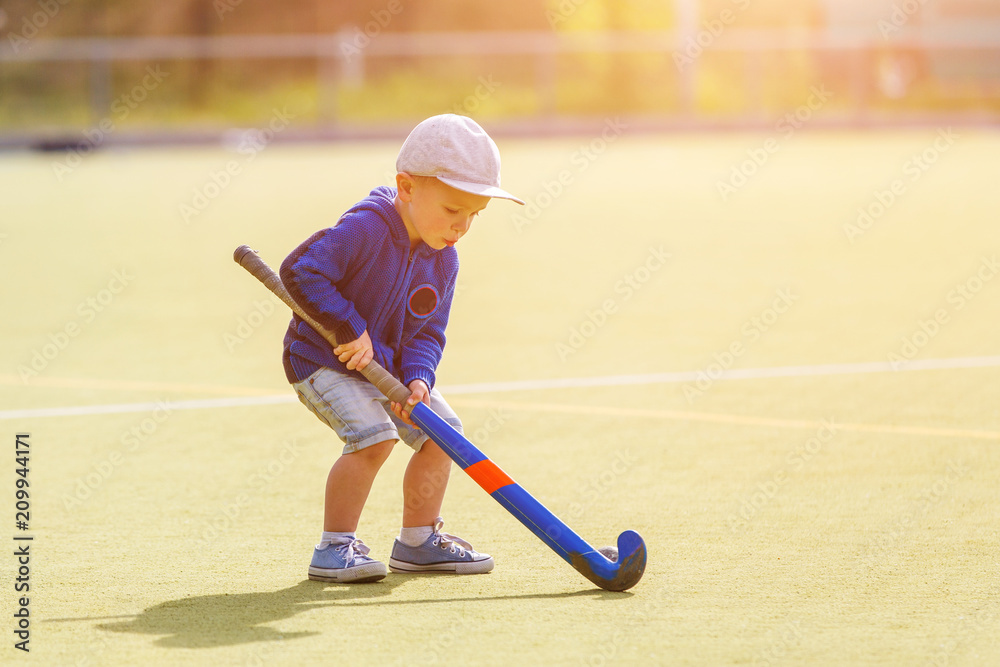 Fototapeta premium Small boy training playing field hockey with stick on the field