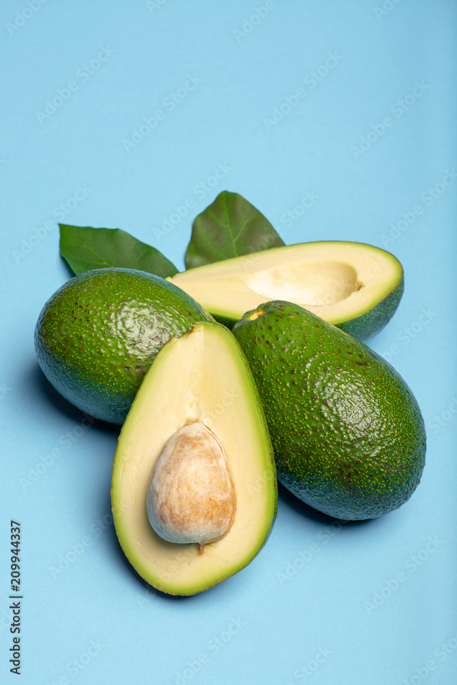 Fresh organic ripe green whole and sliced Fuerte avocado with leaves, copy space close up isolated on trendy blue background