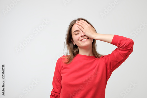 Pleased Caucasian woman wearing red sweater smiling and keeping hand on her cheek