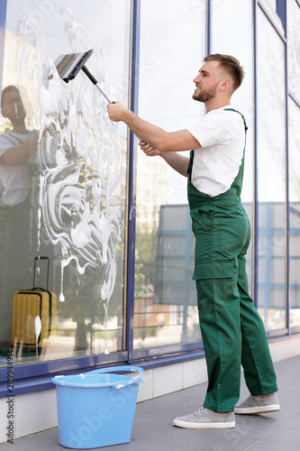 Male cleaner wiping window glass with squeegee from outside
