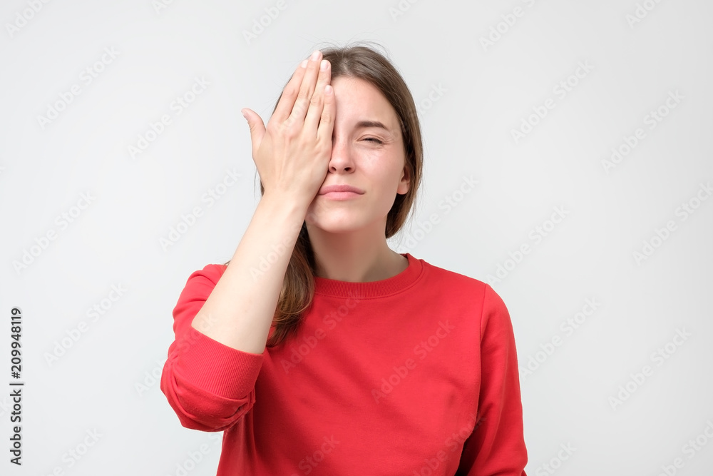 Caucasian woman in red sweater checking her eyesight closing one eye with hand Caucasian woman in red sweater checking her eyesight closing one eye with hand