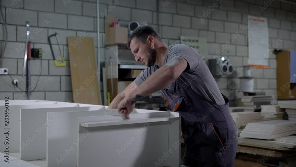 Professional industrial worker in a uniform assembling a furniture in workshop. Professional industrial worker in a uniform assembling a furniture in workshop.