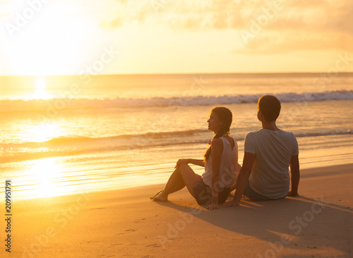 sunset silhouette of young couple in love sitting at beach