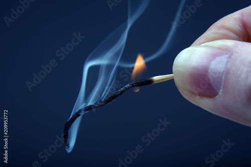 Burning and smoking wooden match in hand on dark background