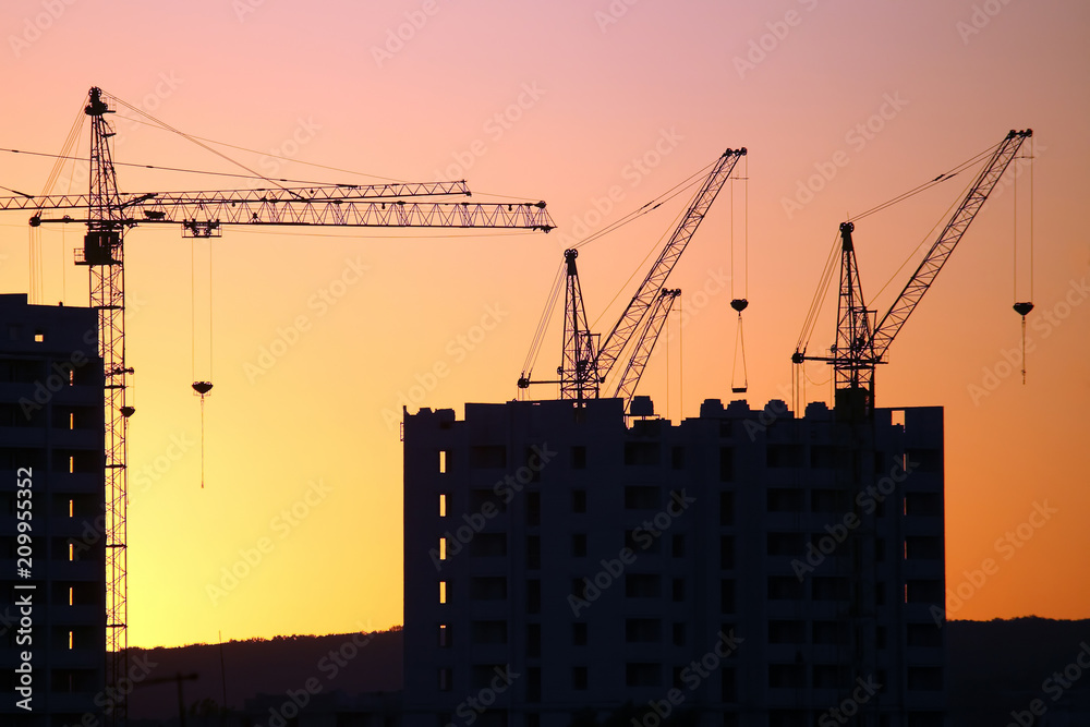 Construction cranes with built houses on the background of the sunset sky