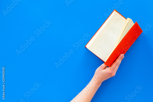 Open the book. Hands hold hardback book opened on blue background top view copy space