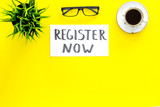 Membership concept. Template for registration. Register now hand lettering iconon word desk with glasses, coffee, plant on yellow background top view space for text