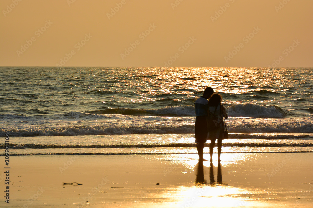 Naklejka premium A man and a woman on the shore of the Arabian sea at sunset on the beach in Northern Goa.India