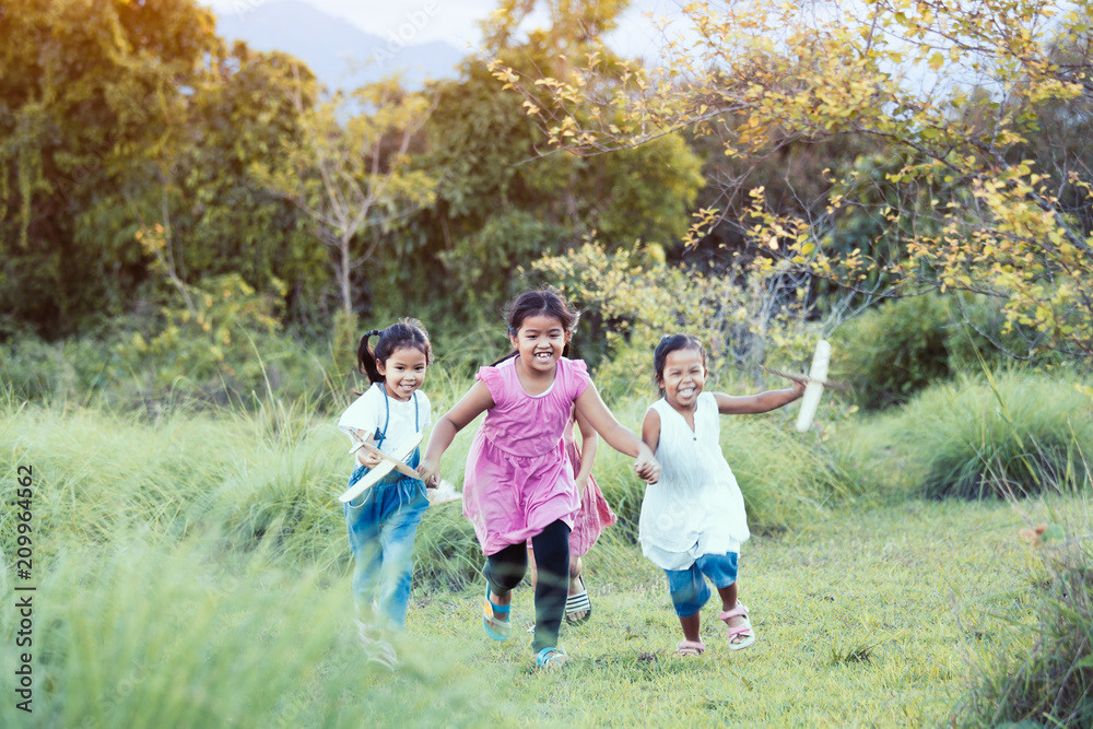 Happy asian children having fun to run and play with toy paper airplane in the meadow  together in summer time