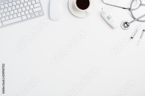 Medical desk with stethoscope,digital thermometer,pen,laptop,mouse and cup of coffee on white desk.Top view with copy space.