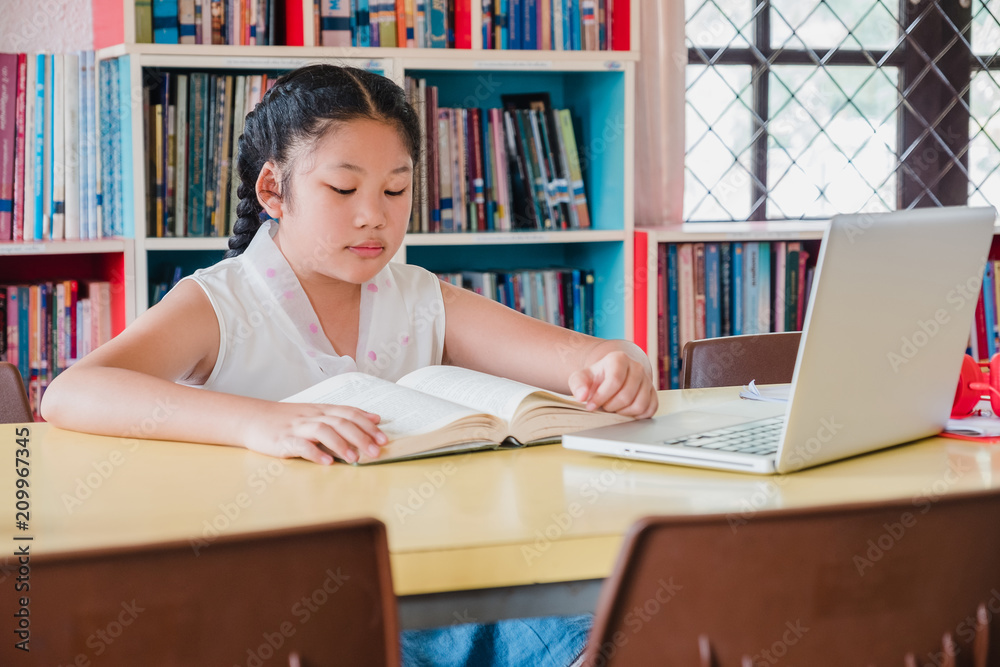 Teenage girl reading book with laptop computer in library.Education and literacy concept Teenage girl reading book with laptop computer in library.Education and literacy concept