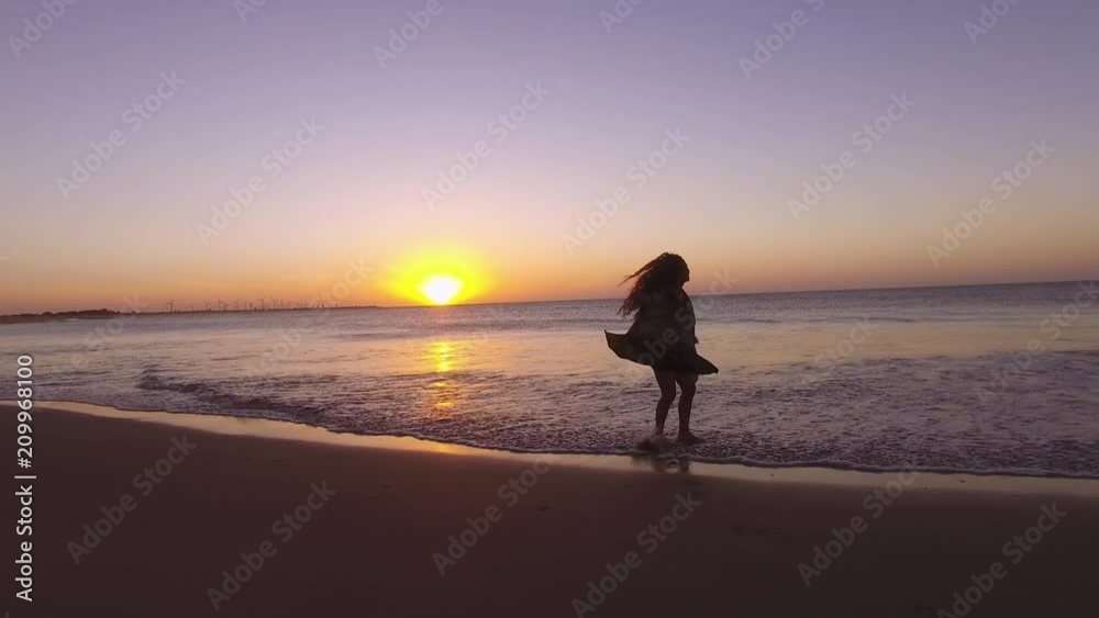 Beautiful happy girl walking/dancing on the beach in an incredible sunset with the sun setting in the sea Beautiful happy girl walking/dancing on the beach in an incredible sunset with the sun setting in the sea