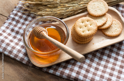 Photo of honey , wooden honey dipper and cracker on wood tray on wood background.