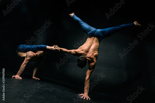 Male acrobatic duo performs a complicated balancing act on a dark background