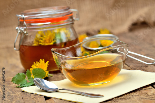 Dandelion honey in glass, spoon, dandelion head around, small colander and full jar in background