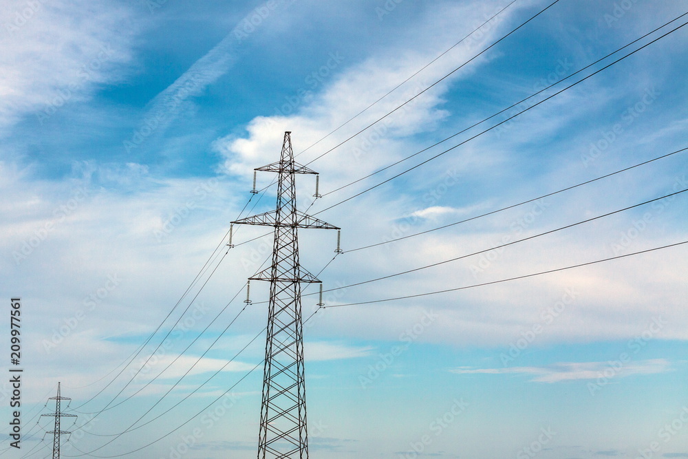 The overhead power line, blue sky and white clouds on the background The overhead power line, blue sky and white clouds on the background