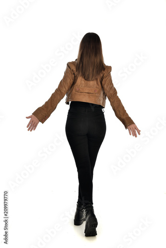 full length portrait of brunette girl wearing brown leather jacket. standing pose with back to the camera on white background.