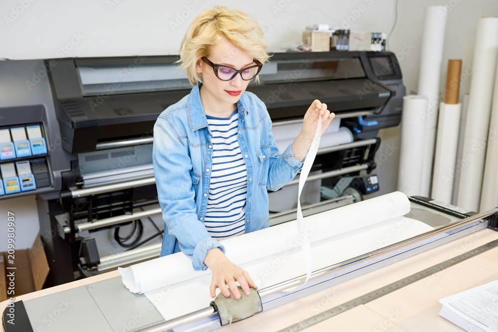 Fotografia Beautiful young woman in glasses printing drafts on plotter during work in office Seventyfour Kup na Posters.pl