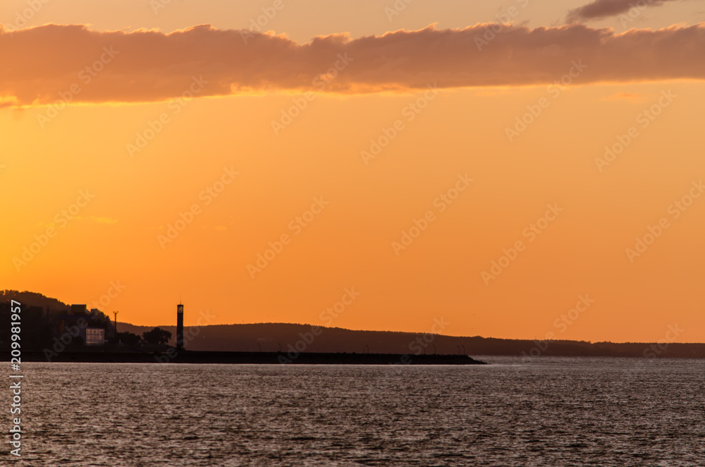 Lighthouse by sea against sky, sunset.