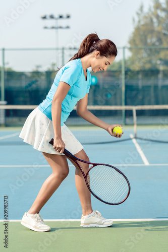Side view of a professional female player smiling while holding the racket and the ball before serving during tennis match © Kzenon