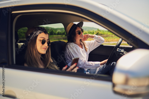 Two girls driving in the car. One girl driving and other using smart phone for text message. © chika_milan