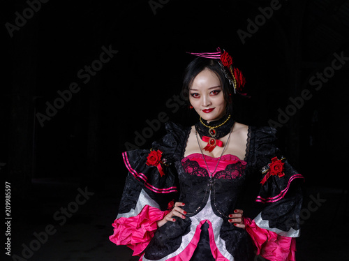 Photo of a female vampire dressed in black and red Longuette, standing on bloody road with red eyes staring at camera, merged in dark background. Halloween, Vampire concept.