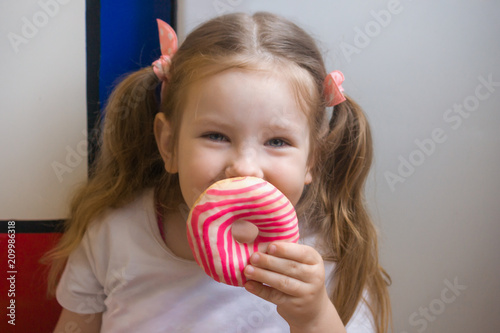 A girl looks at a beautiful glazed donut before eating. She likes to hide part of her face behind a donut. A child plays with food