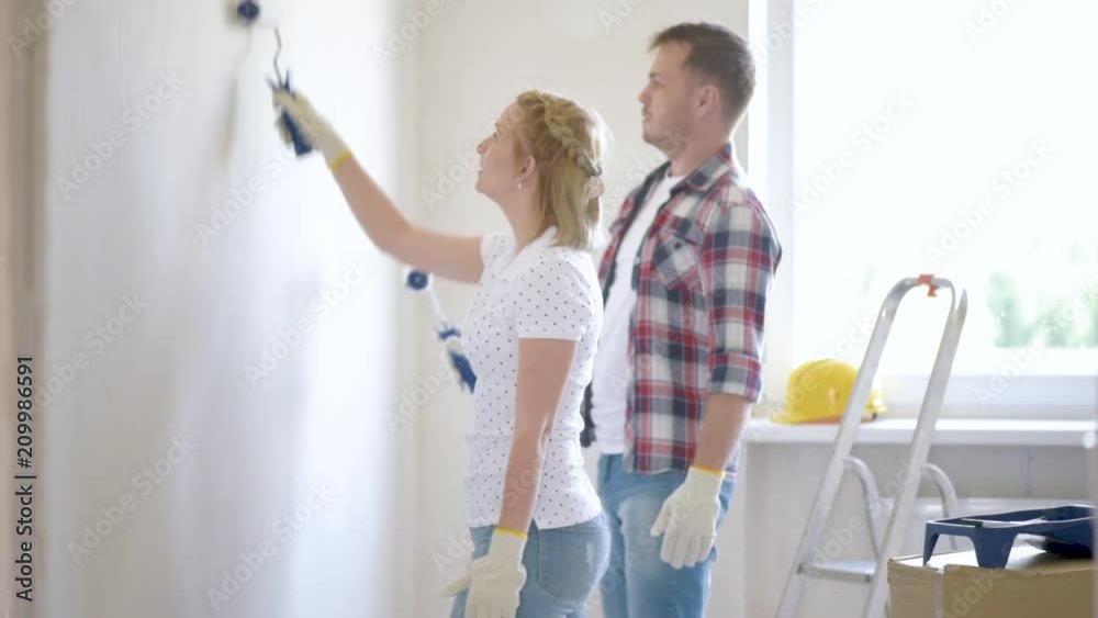 Young family makes repairs in new flat. Beautiful couple - painting wall in apartment. Man and woman doing overhaul of house. Guy and girl making decorate room, laughing and having fun. Young family makes repairs in new flat. Beautiful couple - painting wall in apartment. Man and woman doing overhaul of house. Guy and girl making decorate room, laughing and having fun.