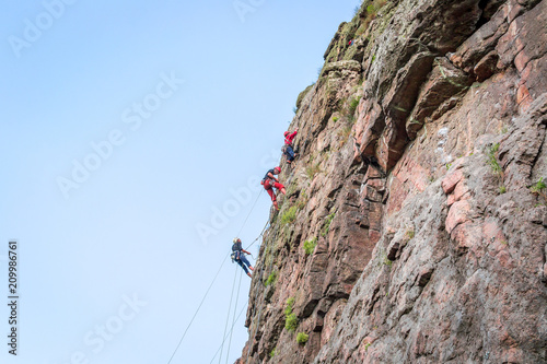 Rock climbing. A group of young rock climbers climb the vertical granite rock. Extreme sport.