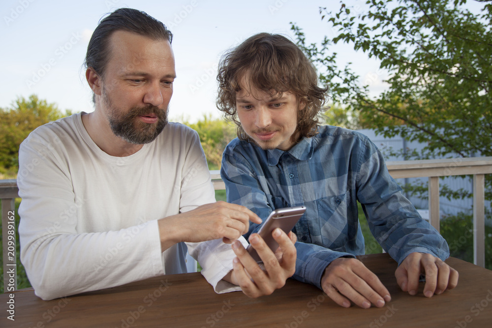 © Chepko Danil - father and son watching the smartphone garden on the terrace on a summer day, family