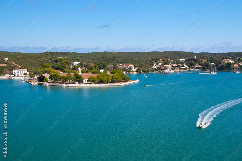 Obraz premium Sea coast of Mahon, Spain. Boats in sea harbor. Naval storehouse and careening wharf. Summer vacation on mediterranean island. Travelling and wanderlust