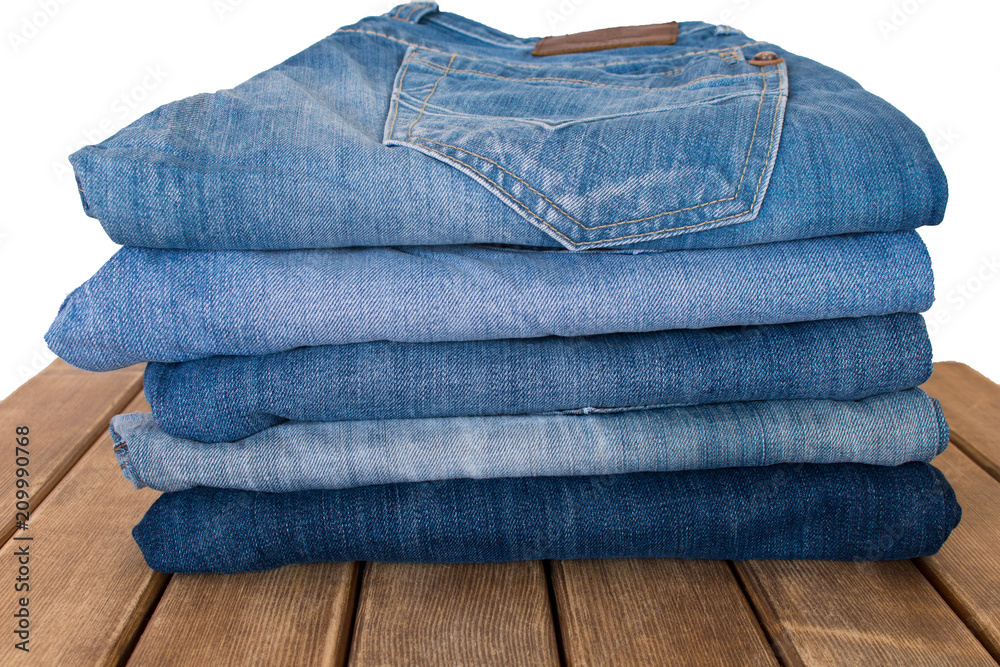A stack of different pairs of blue jeans on a wooden table . Always in trend A stack of different pairs of blue jeans on a wooden table . Always in trend