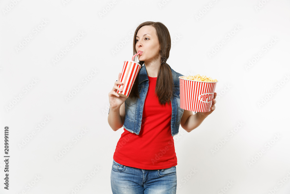 Portrait of young beautiful woman watching movie film, holding bucket of popcorn, drinking from plastic cup of soda or cola looking aside on copy space isolated white background. Emotions in cinema. Portrait of young beautiful woman watching movie film, holding bucket of popcorn, drinking from plastic cup of soda or cola looking aside on copy space isolated white background. Emotions in cinema.