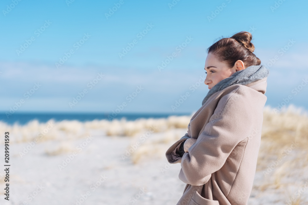 Woman in coat standing at beach on sunny day