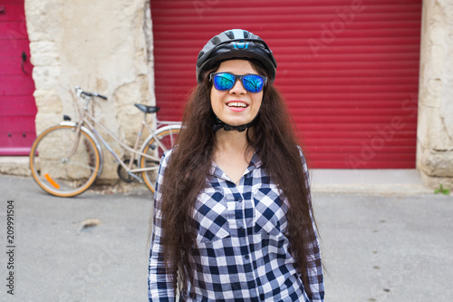 Cheerful woman with sunglasses and helmet on the background red door and bicycle photo