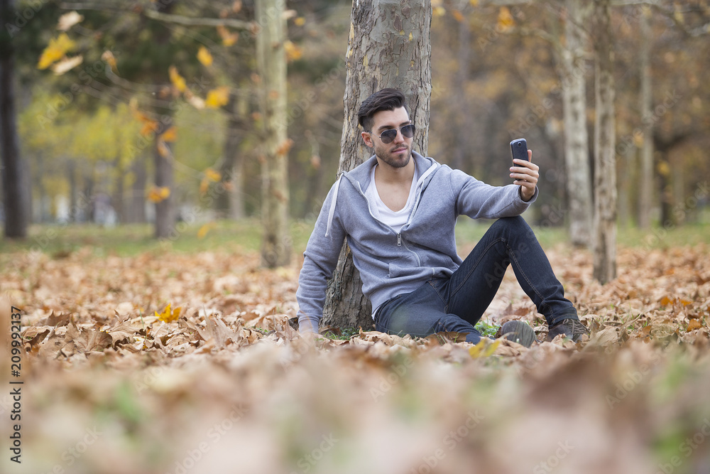Handsome man in nature taking selfie pictures with his smartphone. Autumn. Copy space Handsome man in nature taking selfie pictures with his smartphone. Autumn. Copy space
