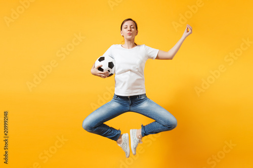 Young fun expressive European woman football fan jumping in air, cheer up support team, holding soccer ball isolated on yellow background. Sport, play football, cheer, fans people lifestyle concept. © ViDi Studio